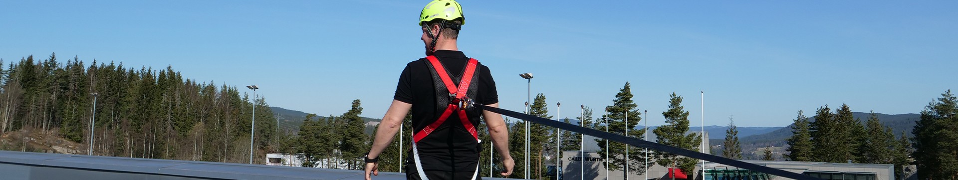 Fallsikringsutstyr vist bak på mann på tak Mann iført fallsikringsutstyr og hjem. Kikker ut fra et tak.